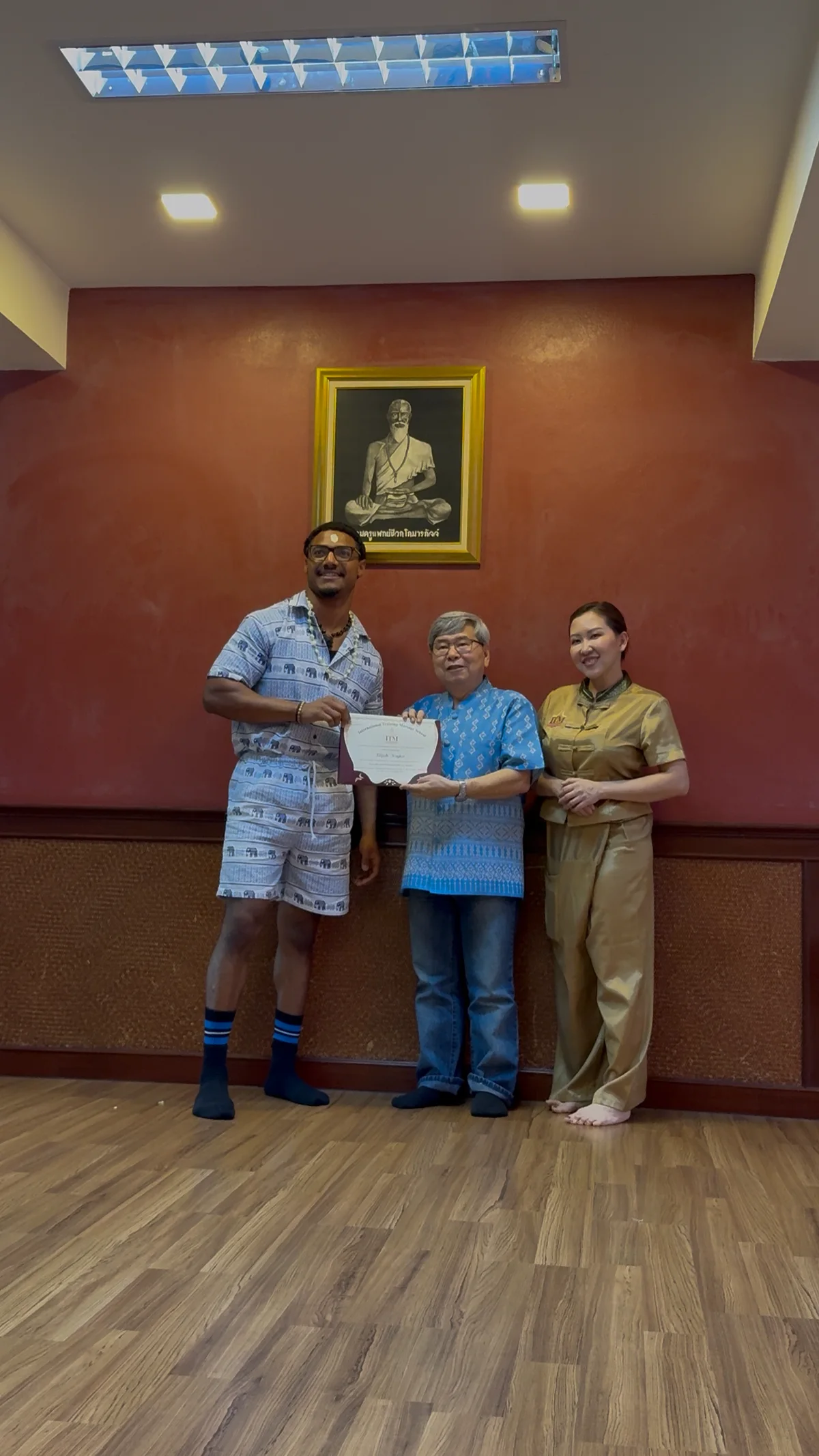 Elijah holding his Thai massage certificate with Master John and Teacher Kate